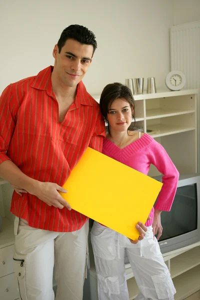 Casal em casa com uma placa em branco — Fotografia de Stock