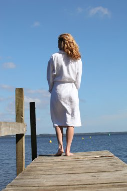Woman in a bathrobe standing on a wooden pier clipart