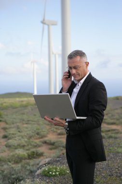 Businessman using his laptop and phone in the middle of nowhere clipart