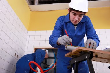 Young plumber cutting grey pipe clipart