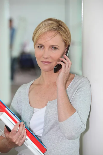 Trabalhador de escritório vestido casualmente com uma pilha de papelada falando em um celular — Fotografia de Stock