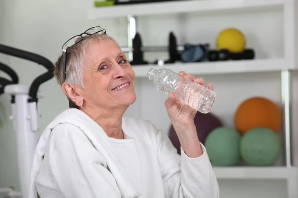 老妇在健身房喝瓶装的水 — 图库照片