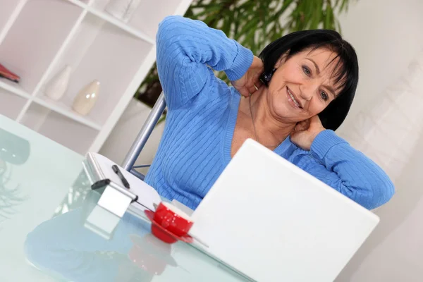 Eine Frau mittleren Alters, die sich vor ihrem Computer dehnt. — Stockfoto
