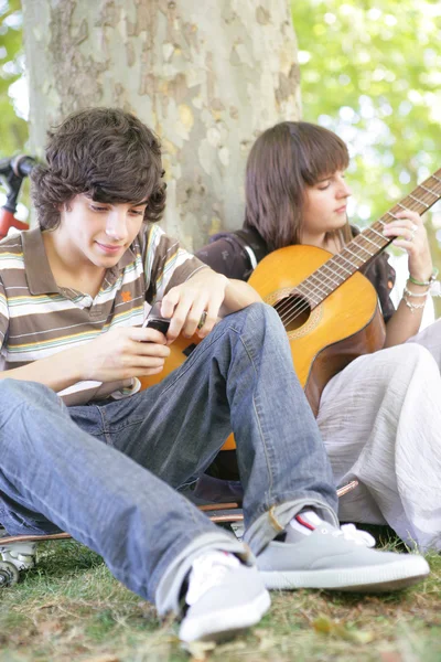 Twee tieners met gitaar zat door boom — Stockfoto