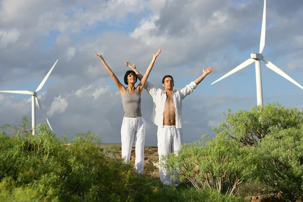 Homem e mulher se estendendo perto de turbinas eólicas — Fotografia de Stock