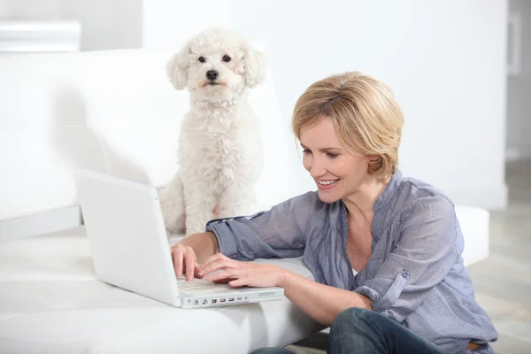 Femme utilisant un ordinateur portable à côté d'un petit chien blanc — Photo
