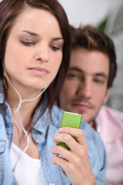 Jovem mulher ouvindo um leitor de MP3 ao lado de seu namorado — Fotografia de Stock