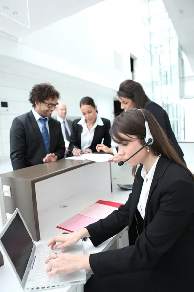 Vrouwelijke receptioniste met behulp van een hoofdtelefoon en laptop computer — Stockfoto