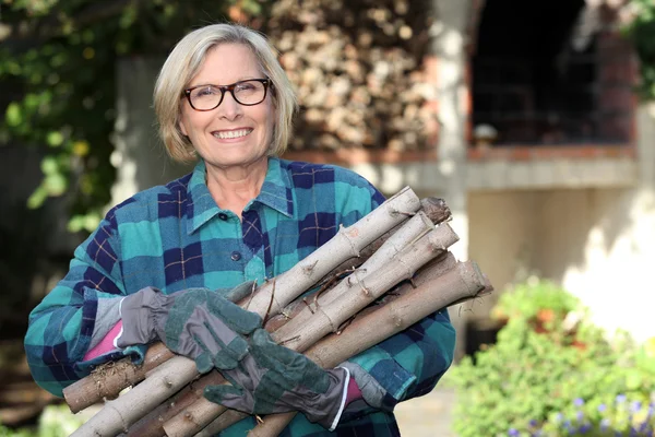 Mulher sênior recolhendo madeira no jardim — Fotografia de Stock