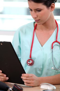 Nurse in scrubs looking at a clipboard clipart