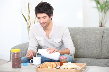 Young man having breakfast in his living room clipart