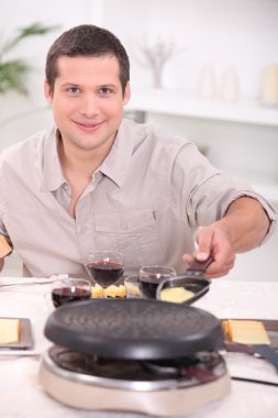 Man cooking raclette at the table clipart