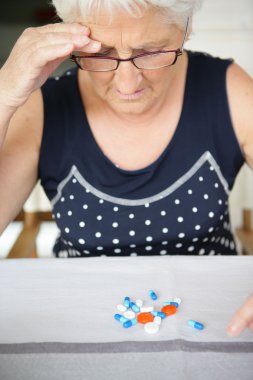 An elderly woman looking at her medication clipart