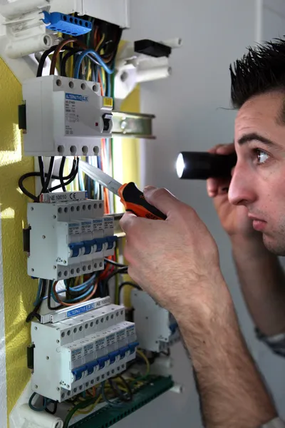 Elettricista che esamina una scatola dei fusibili con una torcia — Foto Stock