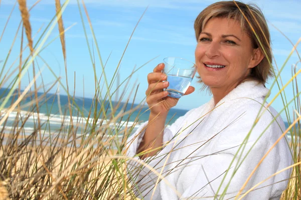 Vrouw drinken van een glas water aan de kust — Stockfoto