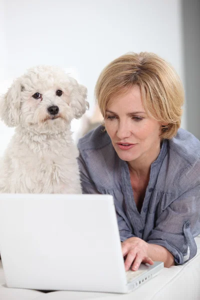 Donna sul computer portatile accompagnata da un piccolo cane bianco — Foto Stock