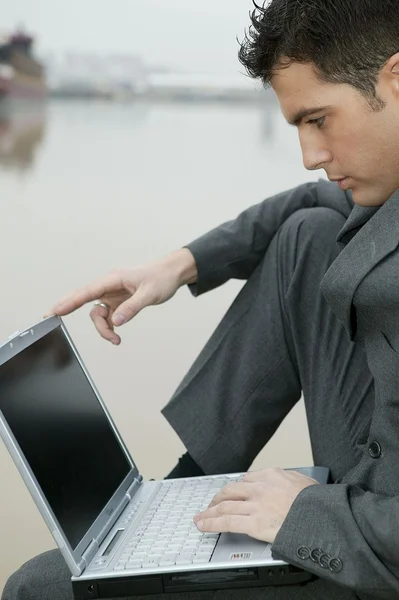 Businessman sat by river using his laptop — Stock Photo, Image