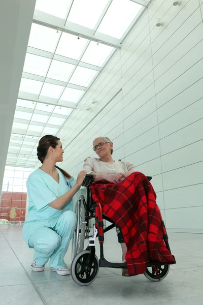 Young brunette nurse and elderly dame in wheel chair in hospital — Stock Photo, Image