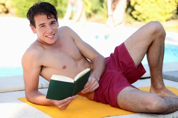 Giovane uomo che legge libro a bordo piscina — Foto Stock