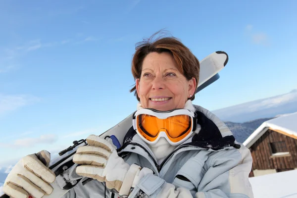 Oudere vrouw skiër buiten een chalet — Stockfoto