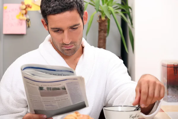 Mann frühstückt gemütlich während er Zeitung liest — Stockfoto