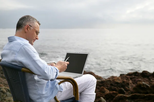 Uomo su una sedia in spiaggia con il suo computer portatile — Foto Stock