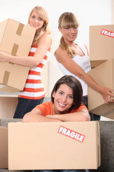 Tres mujeres jóvenes moviendo cajas de cartón marcadas frágiles —  Fotos de Stock