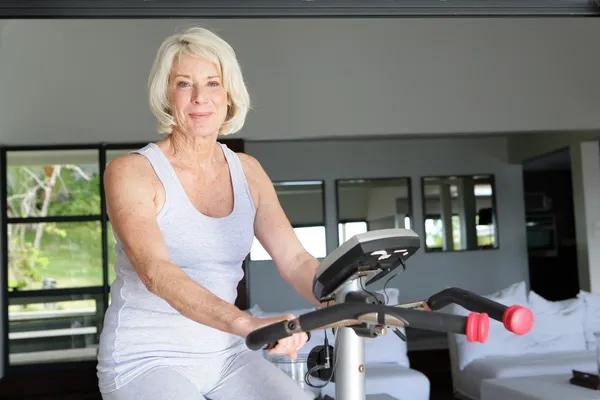 Mature woman using an exercise bike at home — Stock Photo, Image