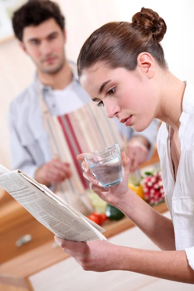 Mujer bebiendo un vaso de agua y leyendo el periódico — Foto de Stock