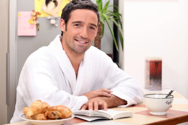 Man reading a book and eating a continental breakfast clipart