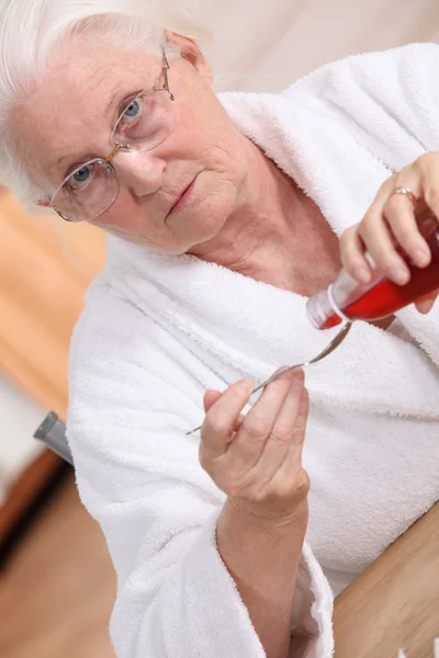 Old woman drinking cough syrup — Stock Photo, Image