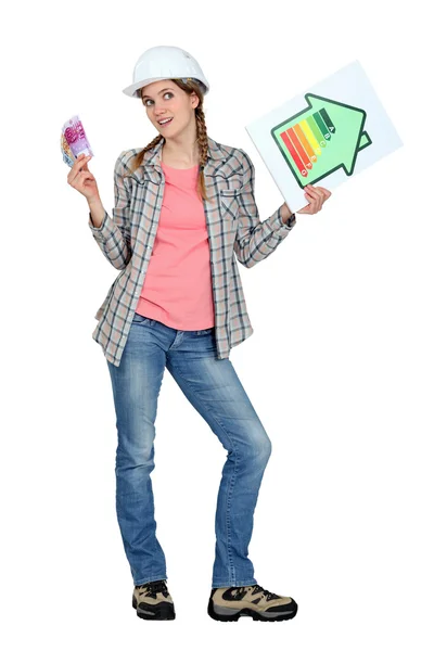 Tradeswoman holding up an energy efficiency rating chart and a wad of money — Stock Photo, Image