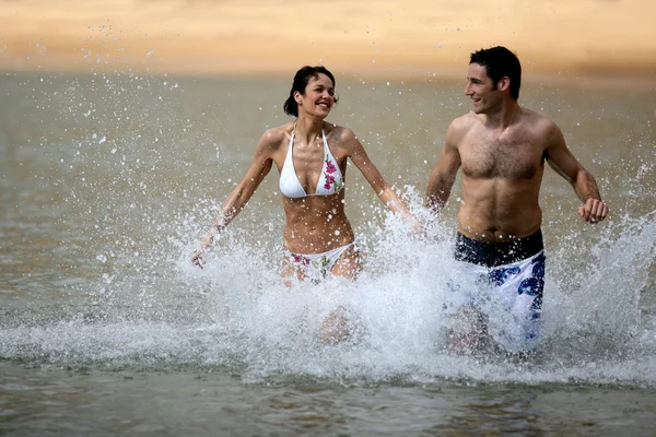 Casal correndo através da água na praia — Fotografia de Stock