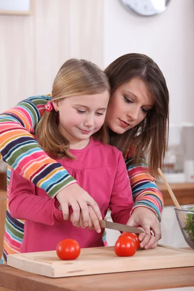 Woman showing her daughter how to cut a tomato — Stock Photo, Image