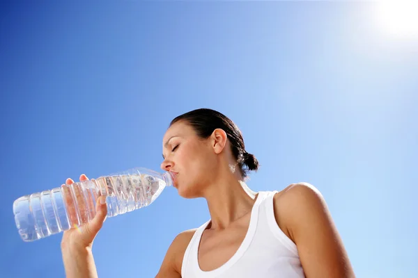 Женщина пьет бутылку воды на фоне голубого неба — стоковое фото
