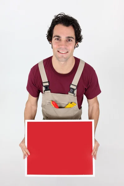 Handyman sosteniendo un tablero rojo dejado en blanco para su mensaje — Foto de Stock