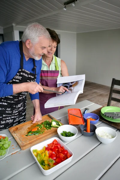 Ηλικιωμένο ζευγάρι που προετοιμάζουμε ένα γεύμα με τη βοήθεια του ένα βιβλίο μαγειρικής — Φωτογραφία Αρχείου