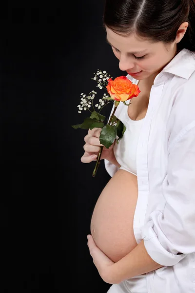 Kobieta w ciąży z różą na czarnym tle — Zdjęcie stockowe