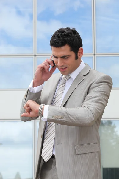 Biznesmen rozmowy na komórkę i sprawdzenie jego zegarek — Zdjęcie stockowe