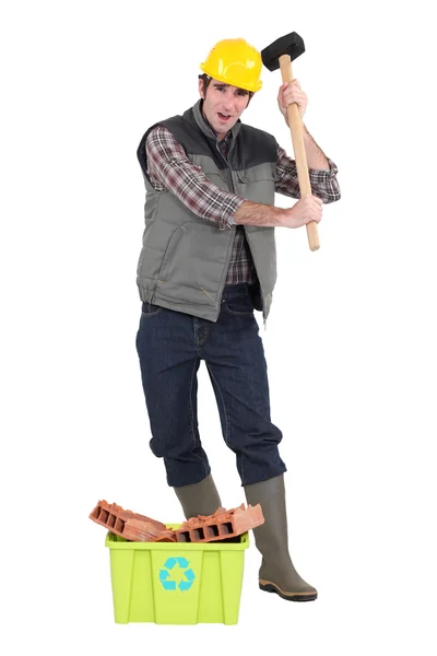 Frustrated tradesman holding a mallet and standing behind a recycling bin — Stock Photo, Image
