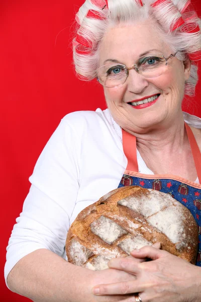 Senior woman with curlers in her hair holding fresh baked bread — Stock Photo, Image