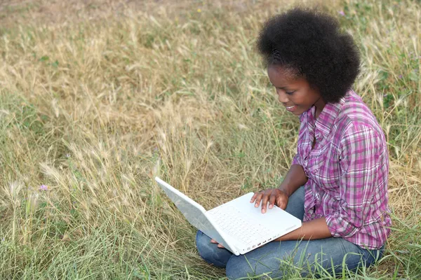 Jovem mulher usando um laptop em um campo — Fotografia de Stock