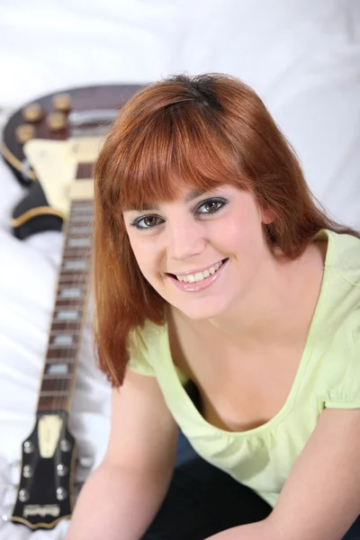 Jovem mulher sentada perto de uma guitarra — Fotografia de Stock