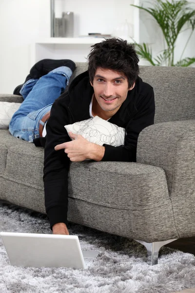 Мужчина лежит на диване со своим ноутбуком — стоковое фото