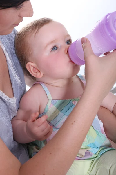 Mamma mata hennes baby vatten från en stor nappflaska — Stockfoto