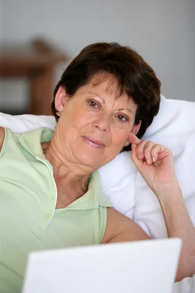 Senior mulher relaxante no sofá com seu laptop — Fotografia de Stock