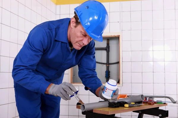 Plumber applying glue to a grey plastic pipe — Stock Photo, Image
