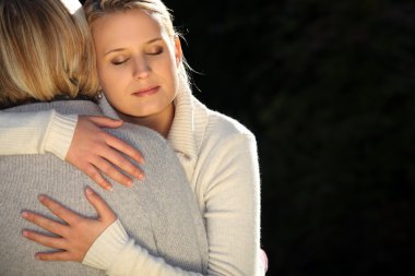 A mother and her teenage daughter hugging. clipart