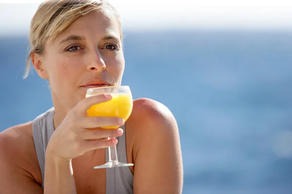 Mujer disfrutando de un vaso de jugo de naranja junto al mar — Foto de Stock