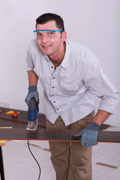 Handwerker trägt Schutzbrille und schneidet ein Stück Holzboden mit — Stockfoto